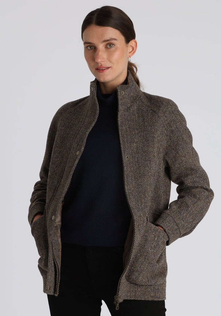 A model wears the Andrea jacket in Harris Tweed, featuring relaxed raglan sleeves, a high neck, generous pockets, and finished with antique brass hardware.