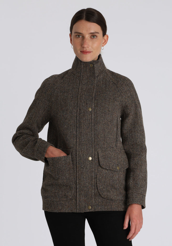 A model wears the Andrea jacket in Harris Tweed, featuring relaxed raglan sleeves, a high neck, generous pockets, and finished with antique brass hardware.