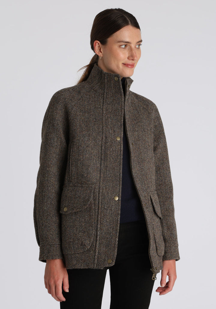 A model wears the Andrea jacket in Harris Tweed, featuring relaxed raglan sleeves, a high neck, generous pockets, and finished with antique brass hardware.