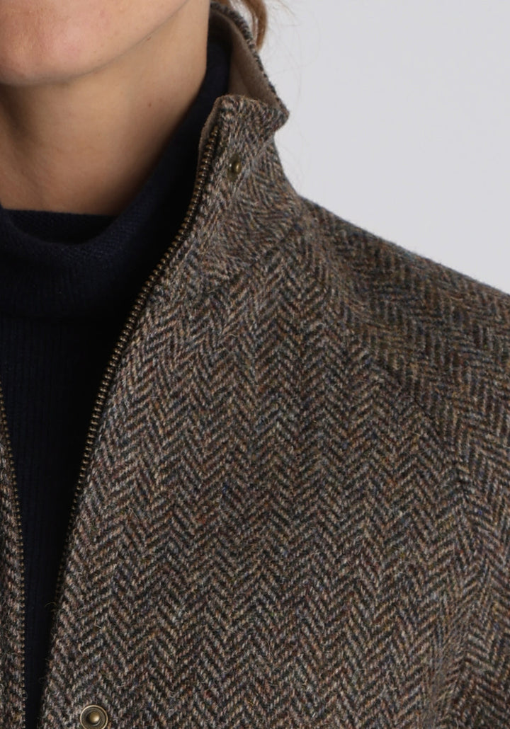 A model wears the Andrea jacket in Harris Tweed, featuring relaxed raglan sleeves, a high neck, generous pockets, and finished with antique brass hardware.