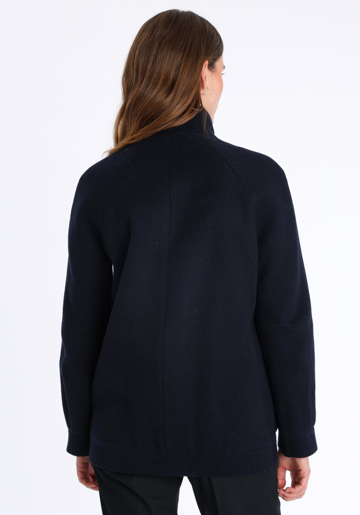 Model wearing the Andrea jacket in navy and rust thick merino wool, a heritage-inspired style with relaxed raglan sleeves, a high neck, and generous pockets, finished with antique brass hardware.