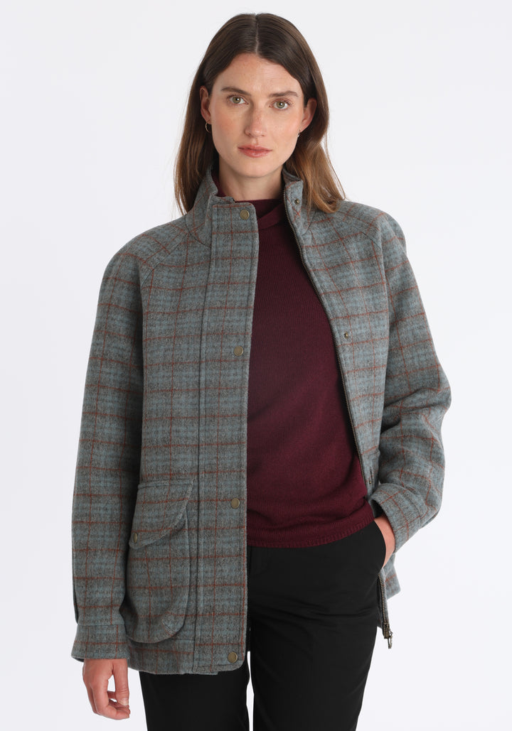 Model wearing the Andrea jacket in silver blue and rust check thick merino wool, a heritage-inspired style with relaxed raglan sleeves, a high neck, and generous pockets, finished with silk velvet trim.