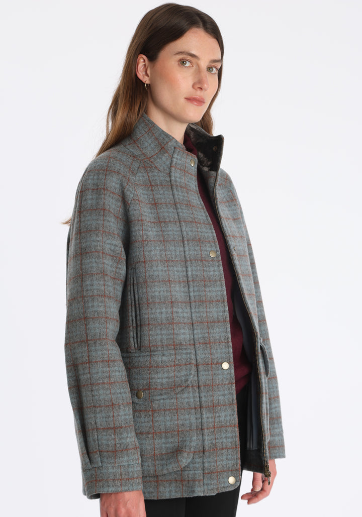 Model wearing the Andrea jacket in silver blue and rust check thick merino wool, a heritage-inspired style with relaxed raglan sleeves, a high neck, and generous pockets, finished with silk velvet trim.
