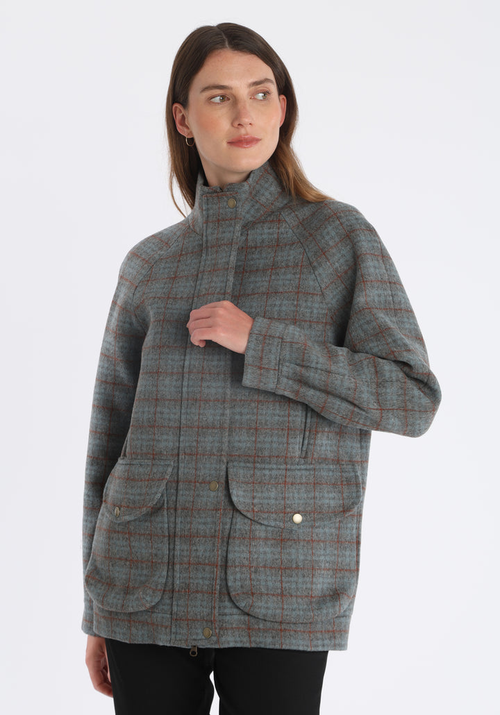 Model wearing the Andrea jacket in silver blue and rust check thick merino wool, a heritage-inspired style with relaxed raglan sleeves, a high neck, and generous pockets, finished with silk velvet trim.