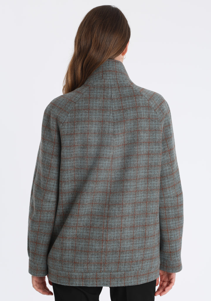 Model wearing the Andrea jacket in silver blue and rust check thick merino wool, a heritage-inspired style with relaxed raglan sleeves, a high neck, and generous pockets, finished with silk velvet trim.