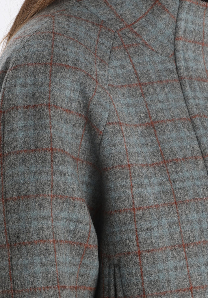 Model wearing the Andrea jacket in silver blue and rust check thick merino wool, a heritage-inspired style with relaxed raglan sleeves, a high neck, and generous pockets, finished with silk velvet trim.