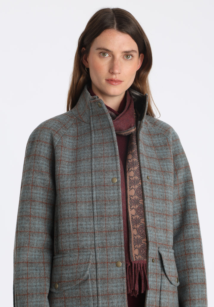 Model wearing the Andrea jacket in silver blue and rust check thick merino wool, a heritage-inspired style with relaxed raglan sleeves, a high neck, and generous pockets, finished with silk velvet trim.