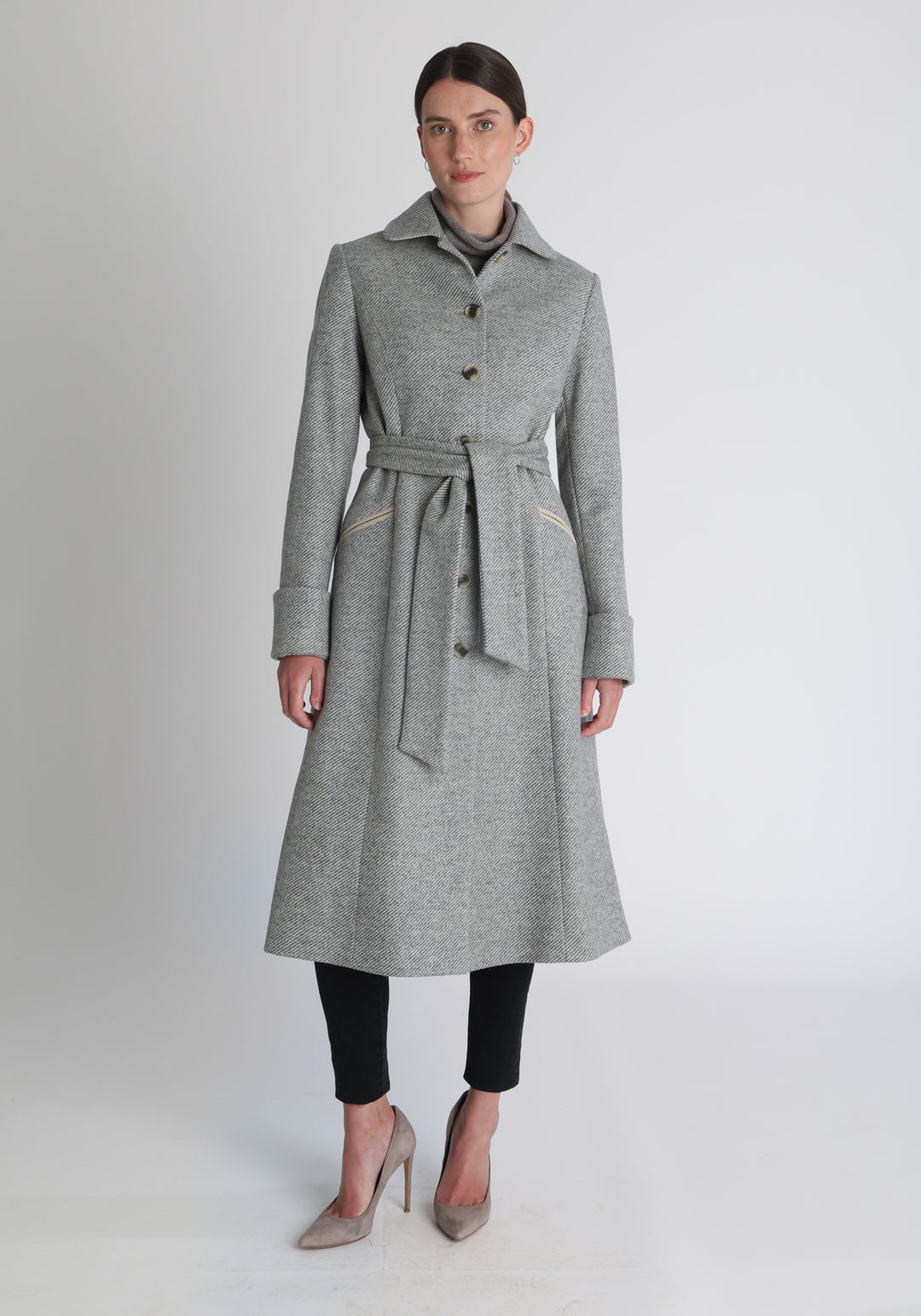Model wearing the Belted coat in slate blue and cream twill lambswool, a long tailored style with a matching belt, turn-back cuffs, and a deep back vent for ease of movement.