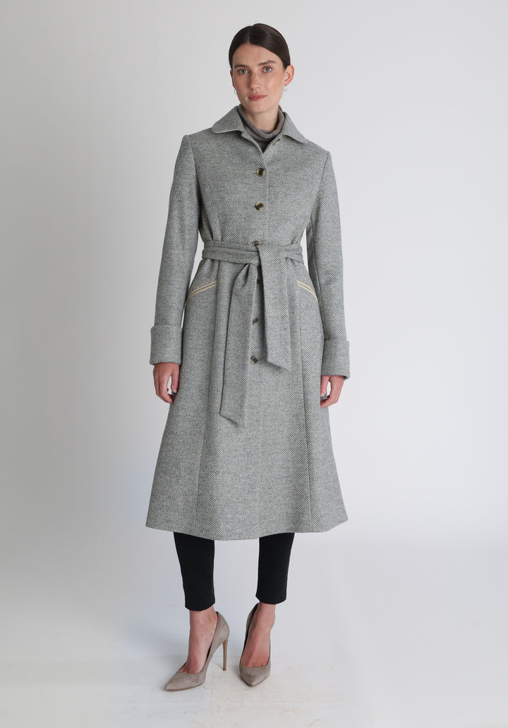 Model wearing the Belted coat in slate blue and cream twill lambswool, a long tailored style with a matching belt, turn-back cuffs, and a deep back vent for ease of movement.