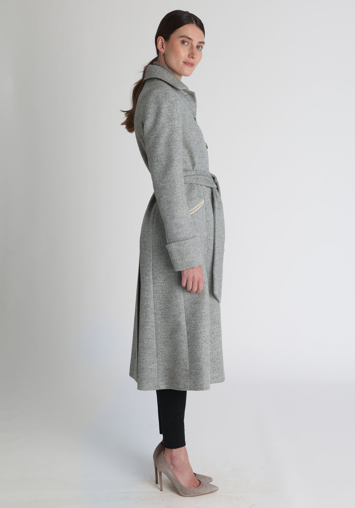 Model wearing the Belted coat in slate blue and cream twill lambswool, a long tailored style with a matching belt, turn-back cuffs, and a deep back vent for ease of movement.
