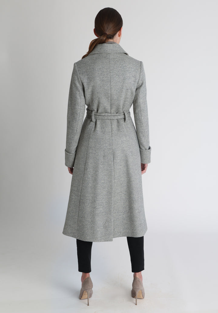 Model wearing the Belted coat in slate blue and cream twill lambswool, a long tailored style with a matching belt, turn-back cuffs, and a deep back vent for ease of movement.