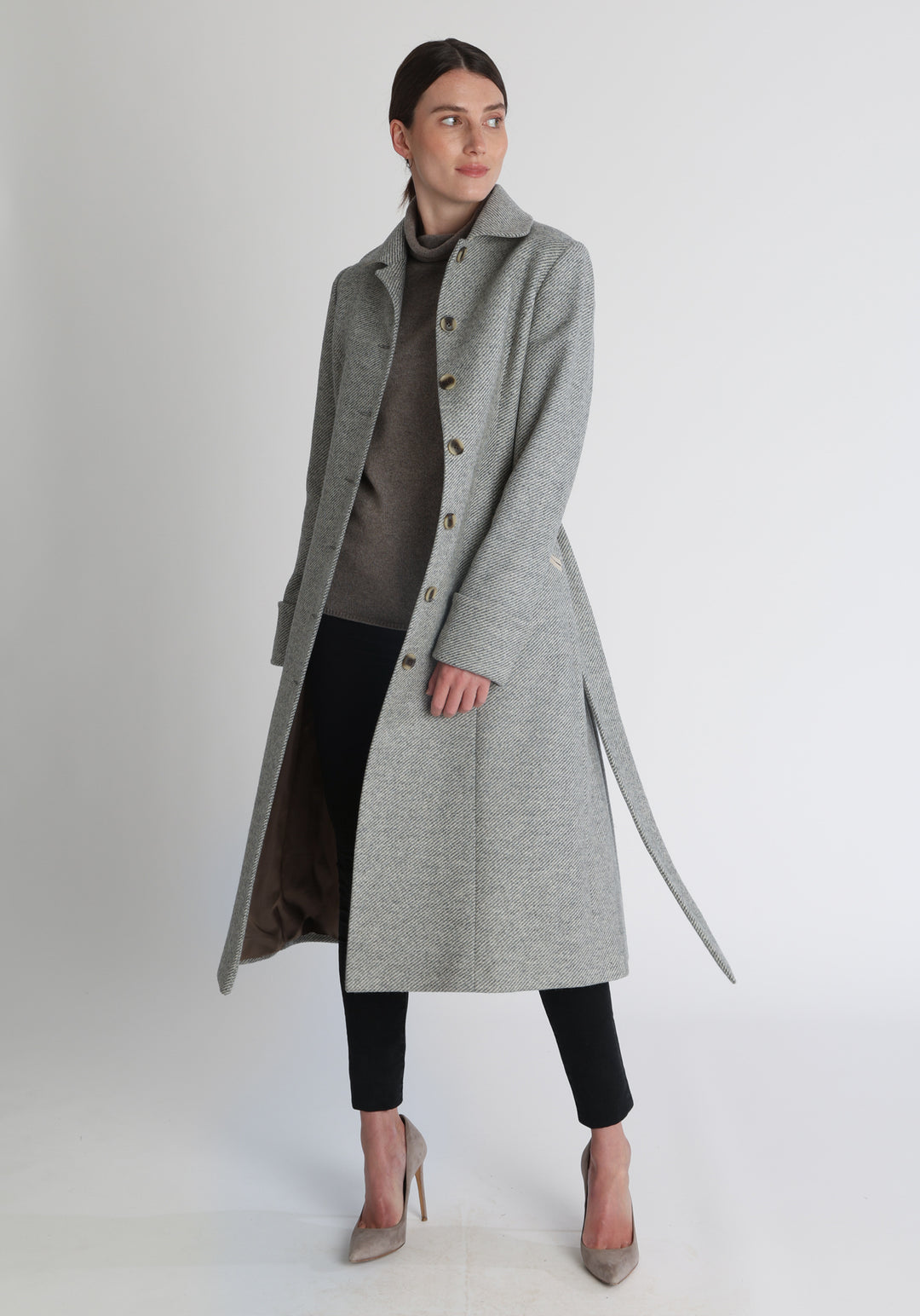 Model wearing the Belted coat in slate blue and cream twill lambswool, a long tailored style with a matching belt, turn-back cuffs, and a deep back vent for ease of movement.