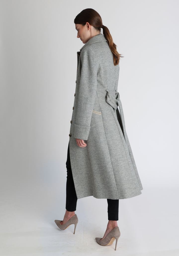 Model wearing the Belted coat in slate blue and cream twill lambswool, a long tailored style with a matching belt, turn-back cuffs, and a deep back vent for ease of movement.