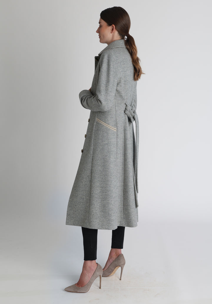 Model wearing the Belted coat in slate blue and cream twill lambswool, a long tailored style with a matching belt, turn-back cuffs, and a deep back vent for ease of movement.