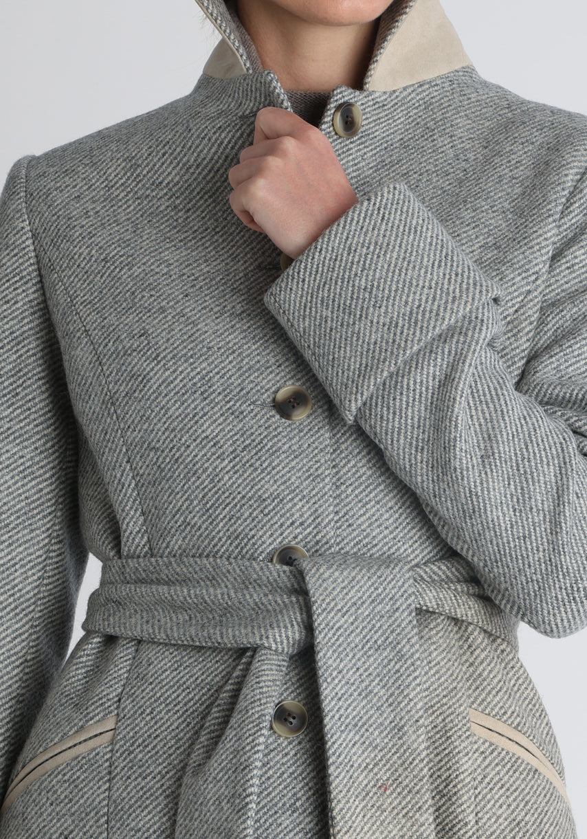 Model wearing the Belted coat in slate blue and cream twill lambswool, a long tailored style with a matching belt, turn-back cuffs, and a deep back vent for ease of movement.