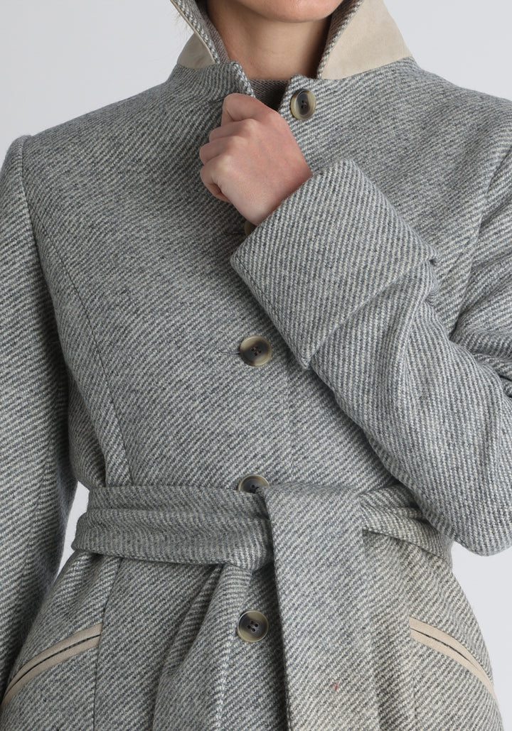 Model wearing the Belted coat in slate blue and cream twill lambswool, a long tailored style with a matching belt, turn-back cuffs, and a deep back vent for ease of movement.