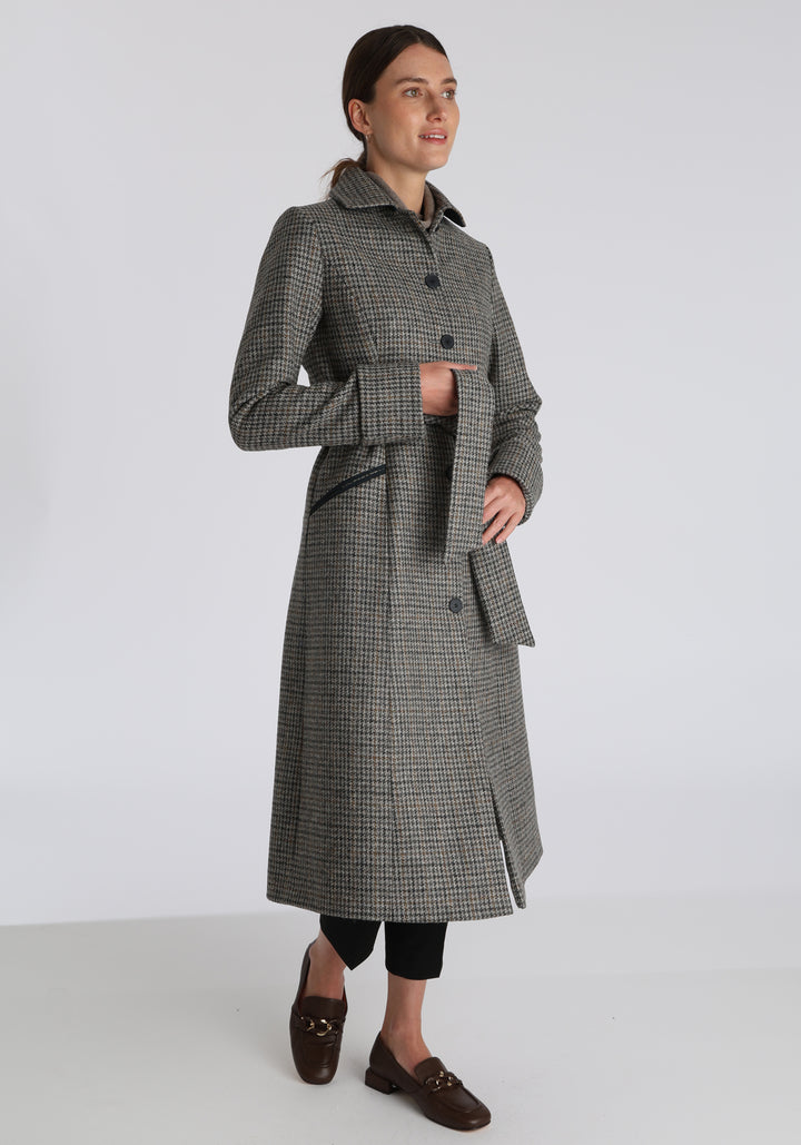 Model wearing the Belted coat in stone grey and ochre dogtooth check wool, a long tailored style with a matching belt, turn-back cuffs, and a deep back vent for ease of movement.