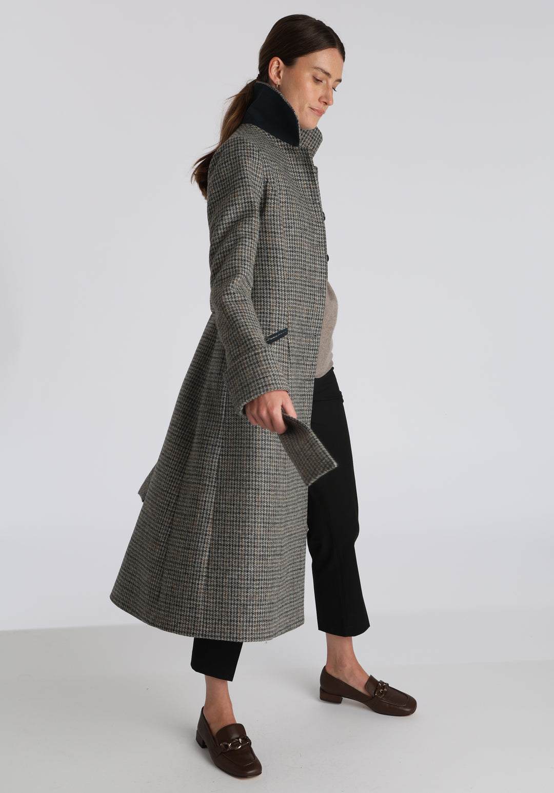 Model wearing the Belted coat in stone grey and ochre dogtooth check wool, a long tailored style with a matching belt, turn-back cuffs, and a deep back vent for ease of movement.