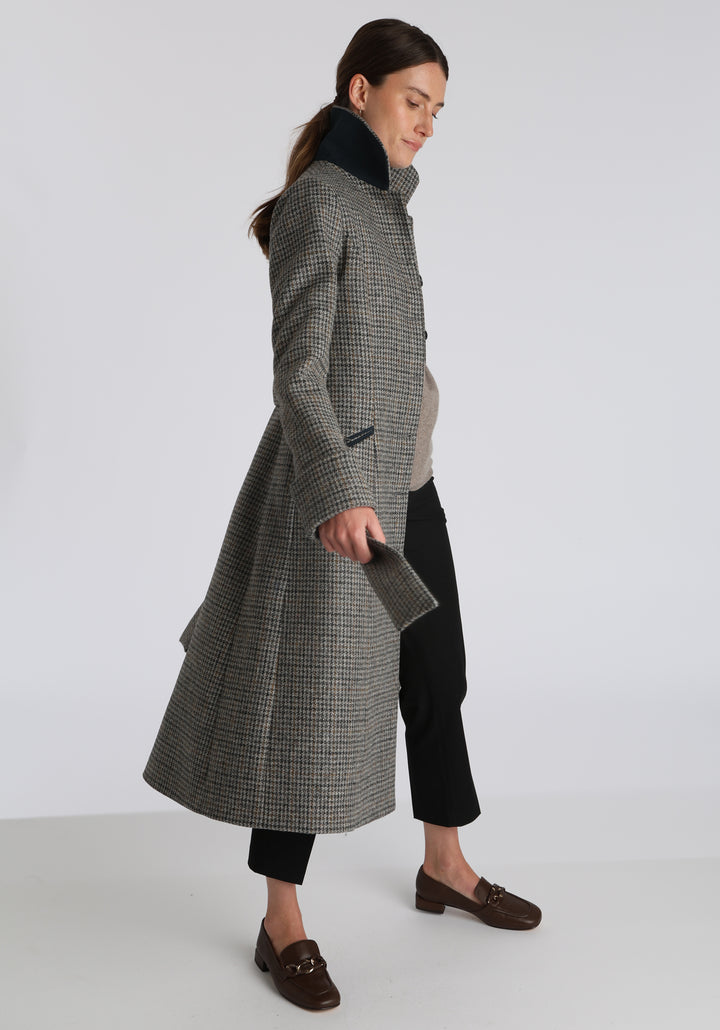 Model wearing the Belted coat in stone grey and ochre dogtooth check wool, a long tailored style with a matching belt, turn-back cuffs, and a deep back vent for ease of movement.