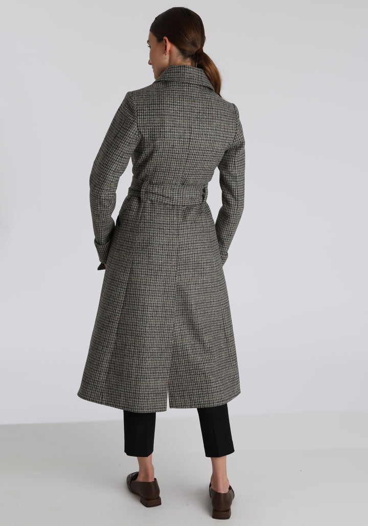Model wearing the Belted coat in stone grey and ochre dogtooth check wool, a long tailored style with a matching belt, turn-back cuffs, and a deep back vent for ease of movement.