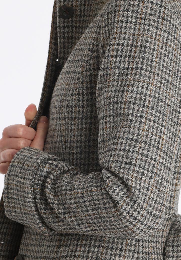 Model wearing the Belted coat in stone grey and ochre dogtooth check wool, a long tailored style with a matching belt, turn-back cuffs, and a deep back vent for ease of movement.