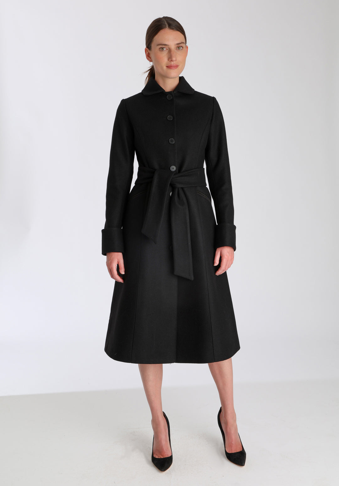 Model wearing the Belted coat in black cashmere blend, a long tailored style with a matching belt, turn-back cuffs, and a deep back vent for ease of movement.