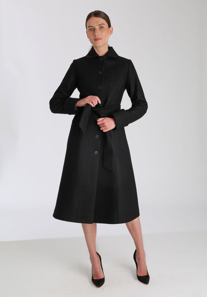 Model wearing the Belted coat in black cashmere blend, a long tailored style with a matching belt, turn-back cuffs, and a deep back vent for ease of movement.