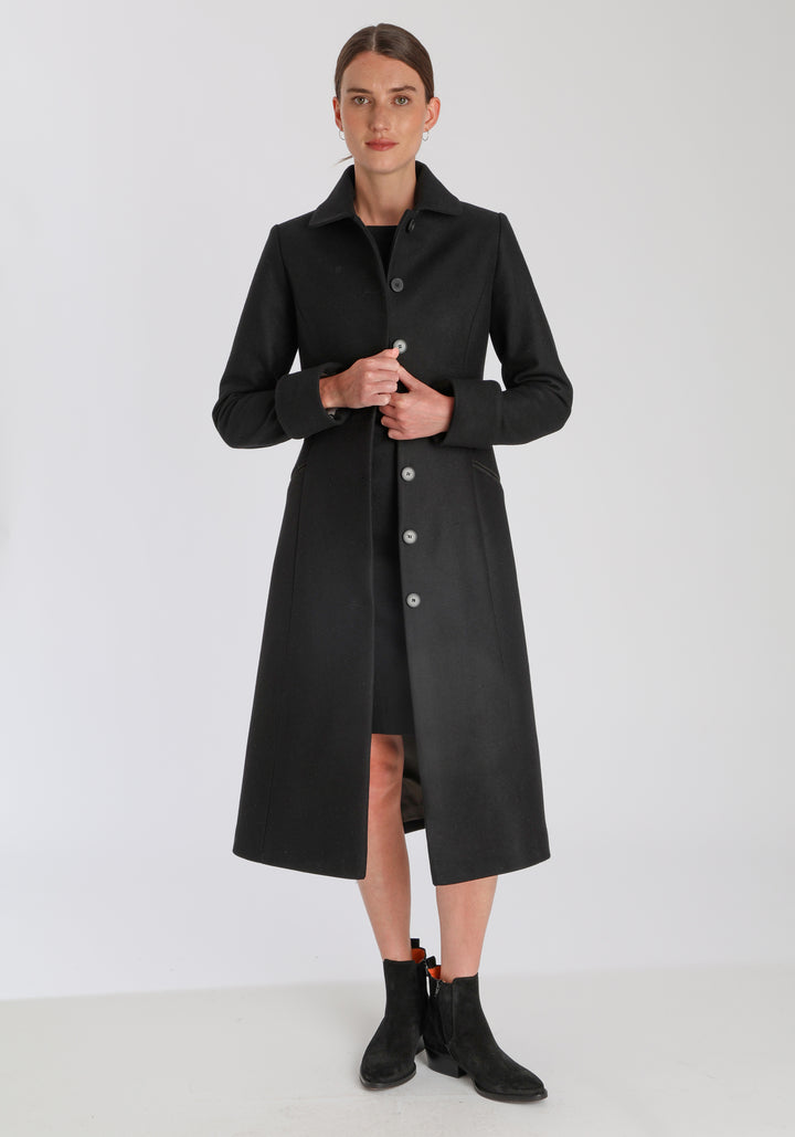 Model wearing the Belted coat in black cashmere blend, a long tailored style with a matching belt, turn-back cuffs, and a deep back vent for ease of movement.
