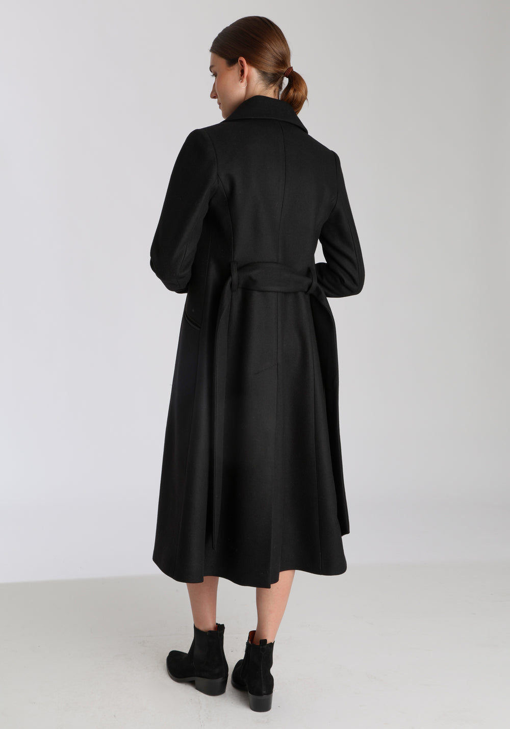 Model wearing the Belted coat in black cashmere blend, a long tailored style with a matching belt, turn-back cuffs, and a deep back vent for ease of movement.