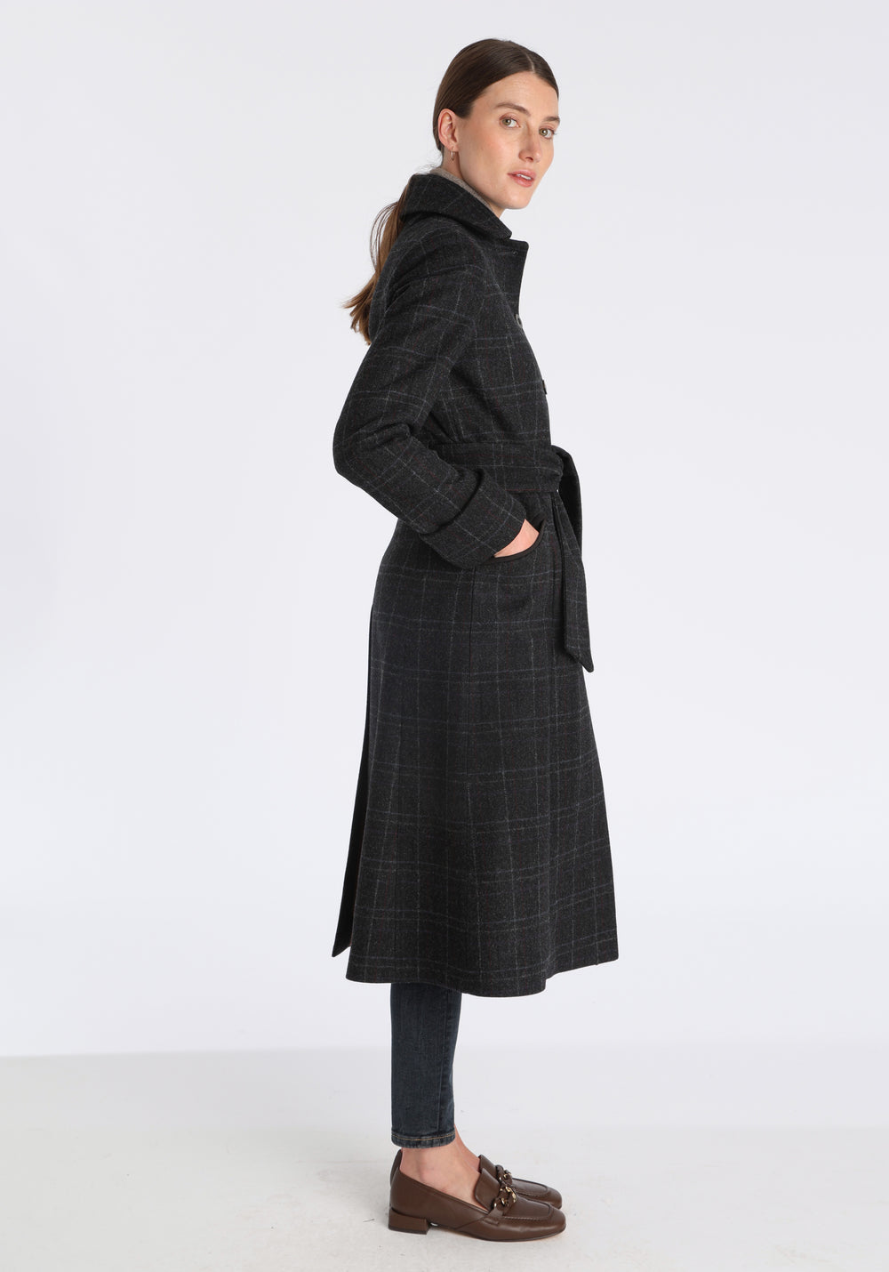 Model wearing the Belted coat in black with faint overcheck, a long tailored style with a matching belt, turn-back cuffs, and a deep back vent for ease of movement.