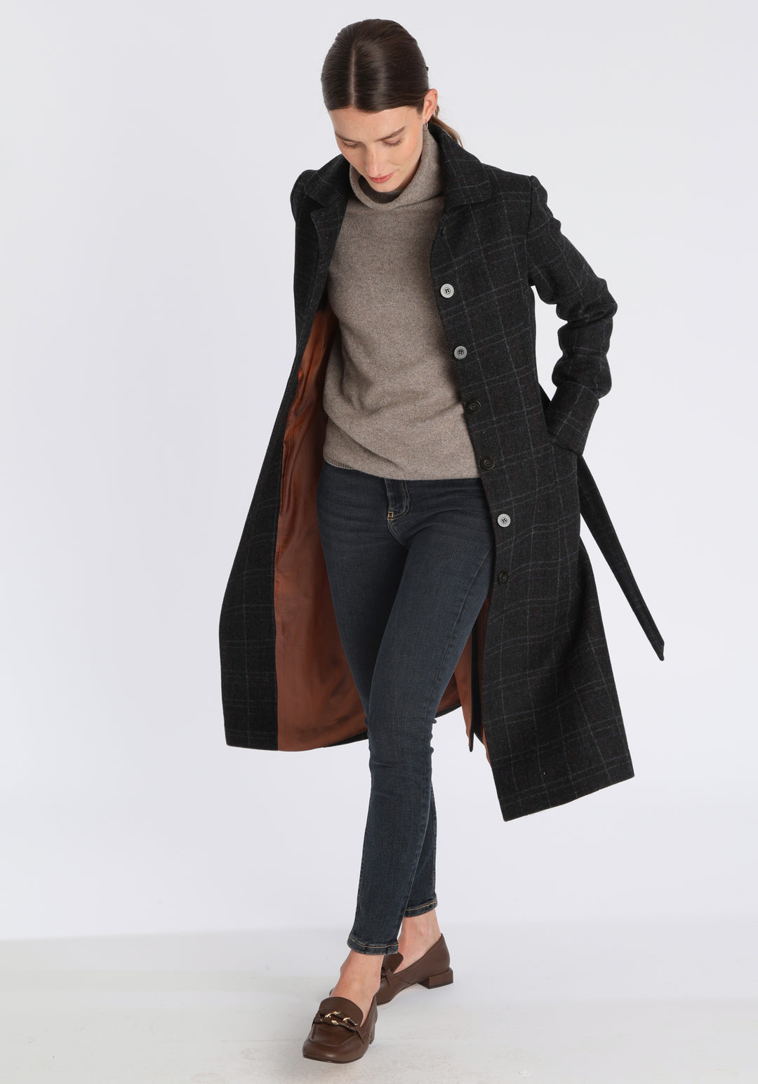 Model wearing the Belted coat in black with faint overcheck, a long tailored style with a matching belt, turn-back cuffs, and a deep back vent for ease of movement.