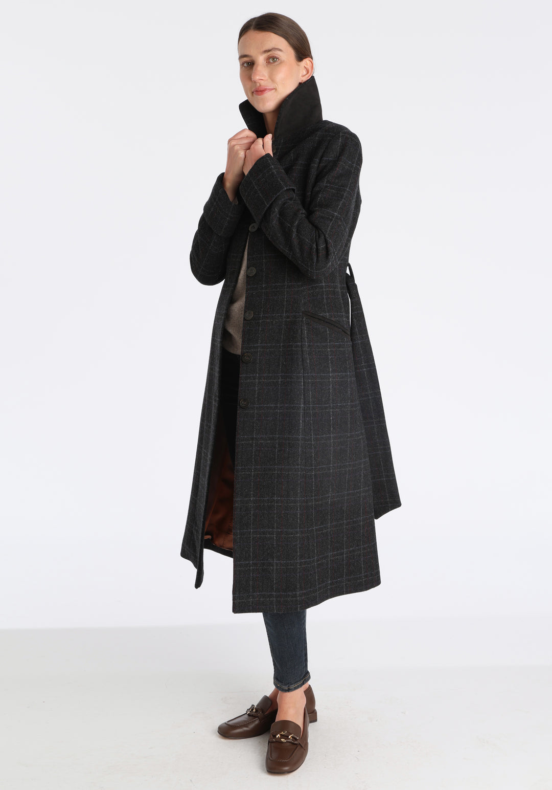 Model wearing the Belted coat in black with faint overcheck, a long tailored style with a matching belt, turn-back cuffs, and a deep back vent for ease of movement.