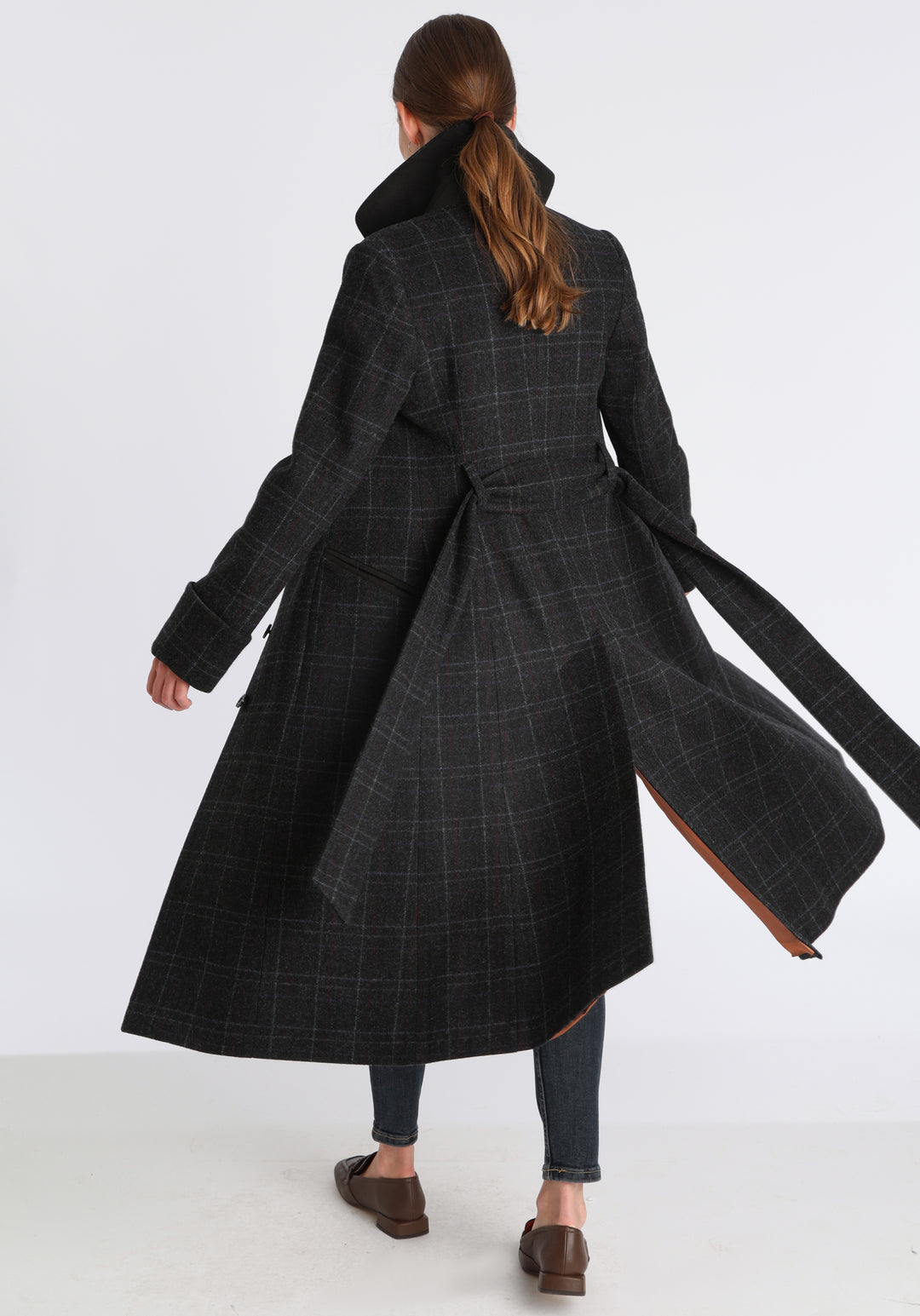 Model wearing the Belted coat in black with faint overcheck, a long tailored style with a matching belt, turn-back cuffs, and a deep back vent for ease of movement.