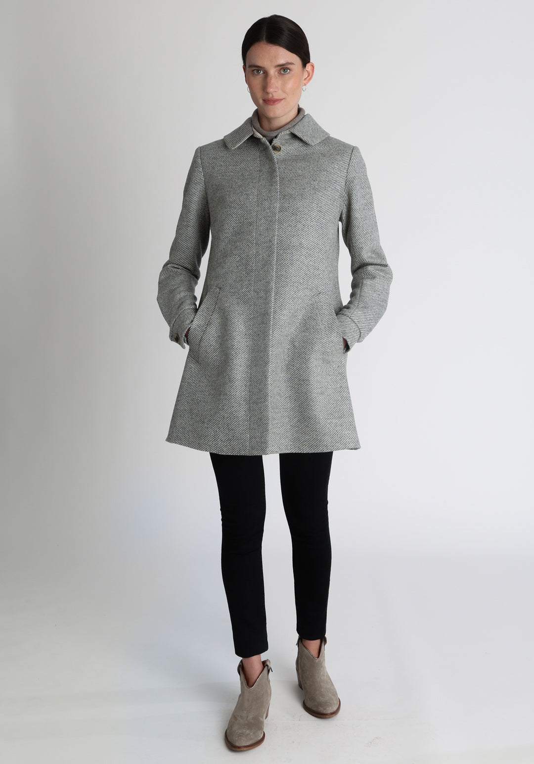 Model wearing the Cape coat in slate blue and cream twill lambswool, a short, structured style with a generous collar, buttoned cuffs, and a deep back pleat that creates a subtle cape like shape.