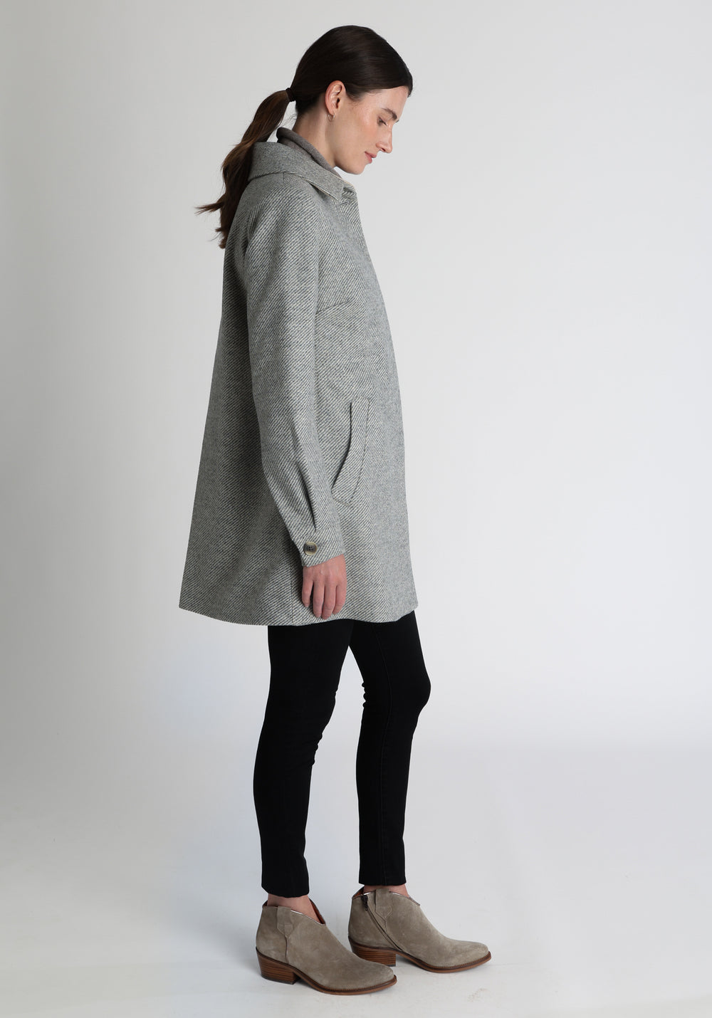 Model wearing the Cape coat in slate blue and cream twill lambswool, a short, structured style with a generous collar, buttoned cuffs, and a deep back pleat that creates a subtle cape like shape.