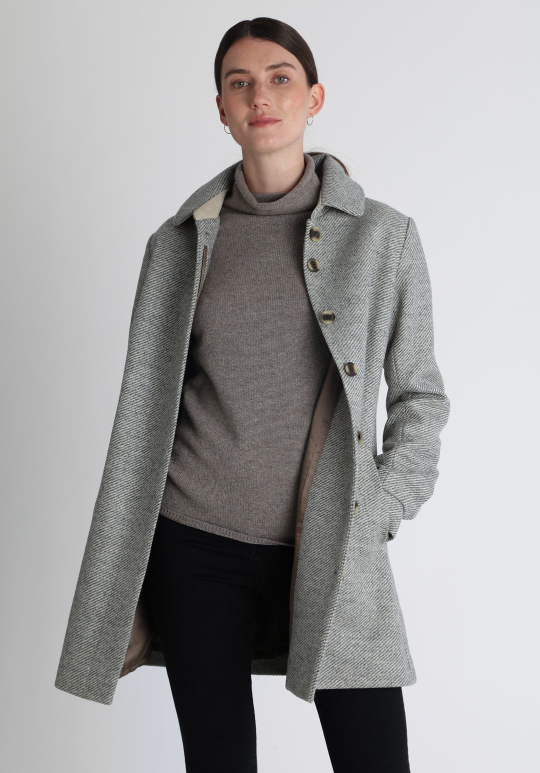 Model wearing the Cape coat in slate blue and cream twill lambswool, a short, structured style with a generous collar, buttoned cuffs, and a deep back pleat that creates a subtle cape like shape.