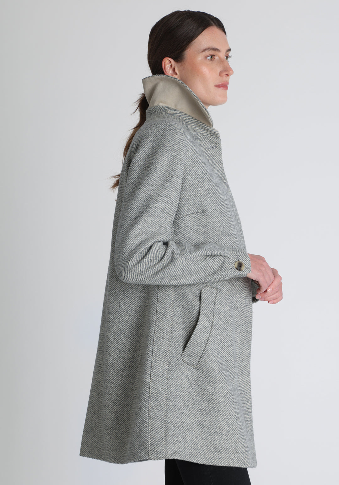 Model wearing the Cape coat in slate blue and cream twill lambswool, a short, structured style with a generous collar, buttoned cuffs, and a deep back pleat that creates a subtle cape like shape.