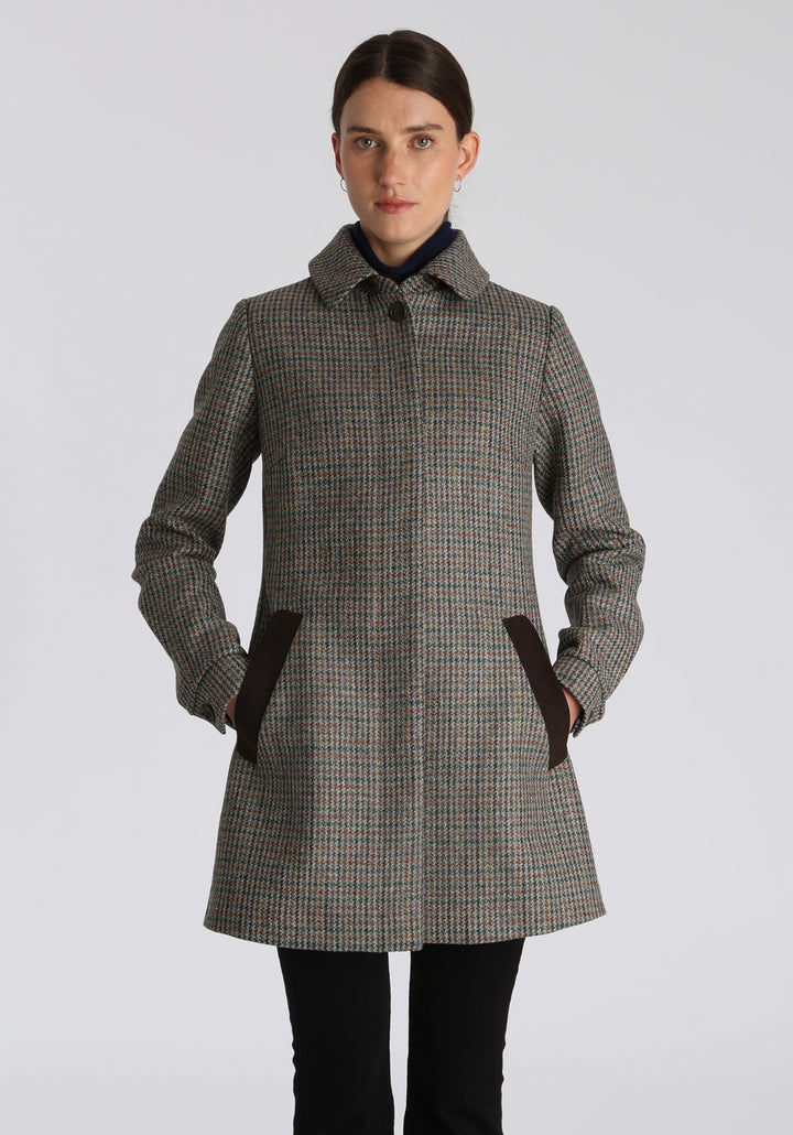 Model wearing the Cape coat in autumnal cinder dogtooth check, a short, structured style with a generous collar, buttoned cuffs, and a deep back pleat that creates a subtle cape-like shape.