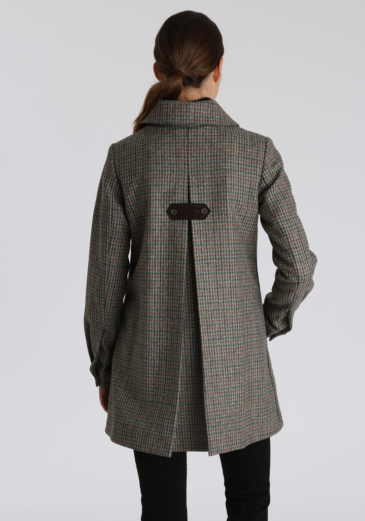 Model wearing the Cape coat in autumnal cinder dogtooth check, a short, structured style with a generous collar, buttoned cuffs, and a deep back pleat that creates a subtle cape-like shape.