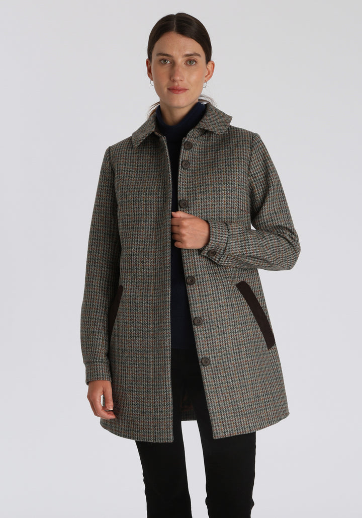Model wearing the Cape coat in autumnal cinder dogtooth check, a short, structured style with a generous collar, buttoned cuffs, and a deep back pleat that creates a subtle cape-like shape.