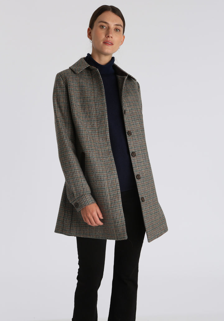 Model wearing the Cape coat in autumnal cinder dogtooth check, a short, structured style with a generous collar, buttoned cuffs, and a deep back pleat that creates a subtle cape-like shape.