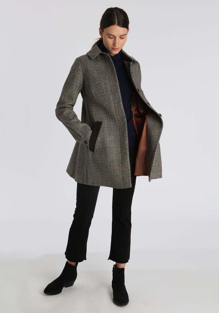 Model wearing the Cape coat in autumnal cinder dogtooth check, a short, structured style with a generous collar, buttoned cuffs, and a deep back pleat that creates a subtle cape-like shape.