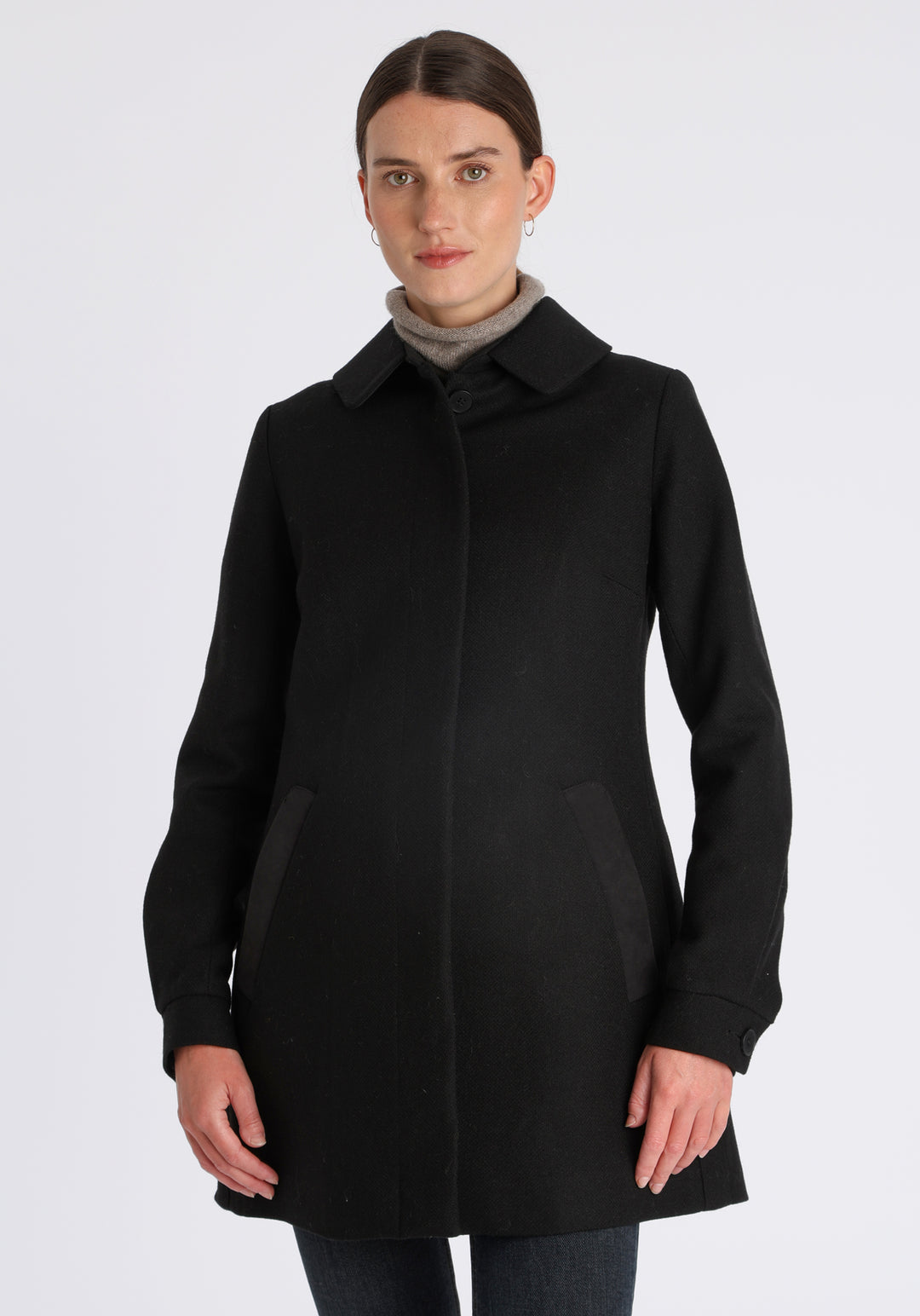 Model wearing the Cape coat in black textured merino wool, a short, structured style with a generous collar, buttoned cuffs, and a deep back pleat that creates a subtle cape-like shape.