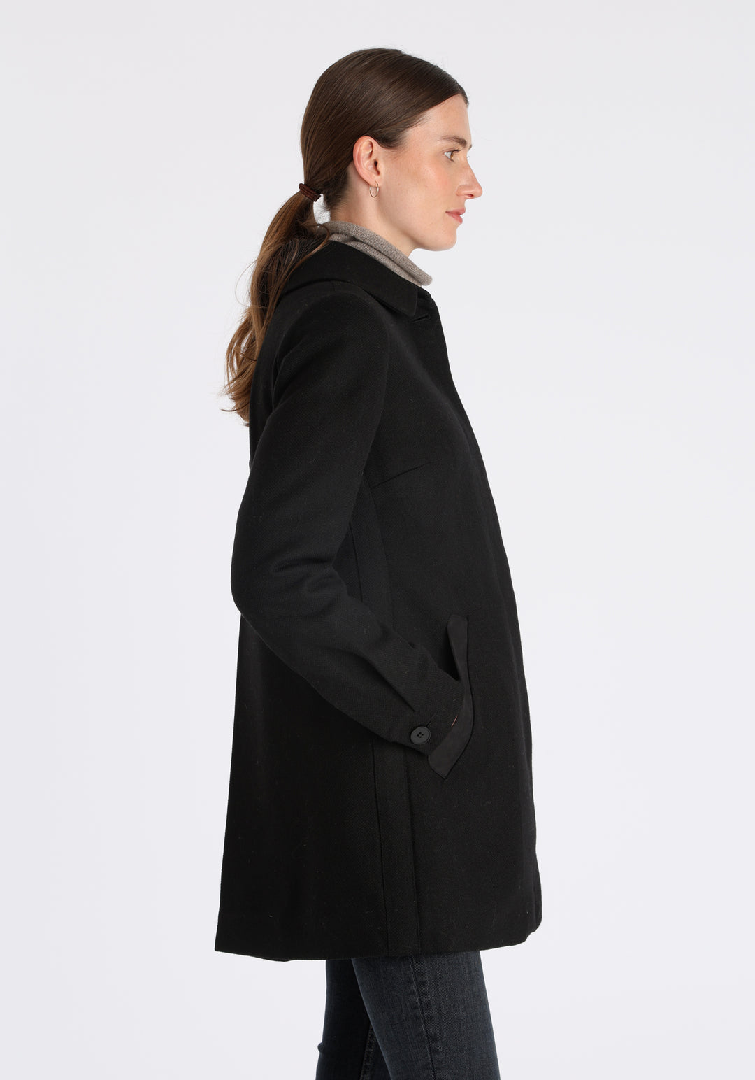 Model wearing the Cape coat in black textured merino wool, a short, structured style with a generous collar, buttoned cuffs, and a deep back pleat that creates a subtle cape-like shape.