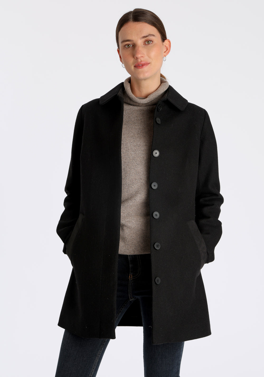 Model wearing the Cape coat in black textured merino wool, a short, structured style with a generous collar, buttoned cuffs, and a deep back pleat that creates a subtle cape-like shape.