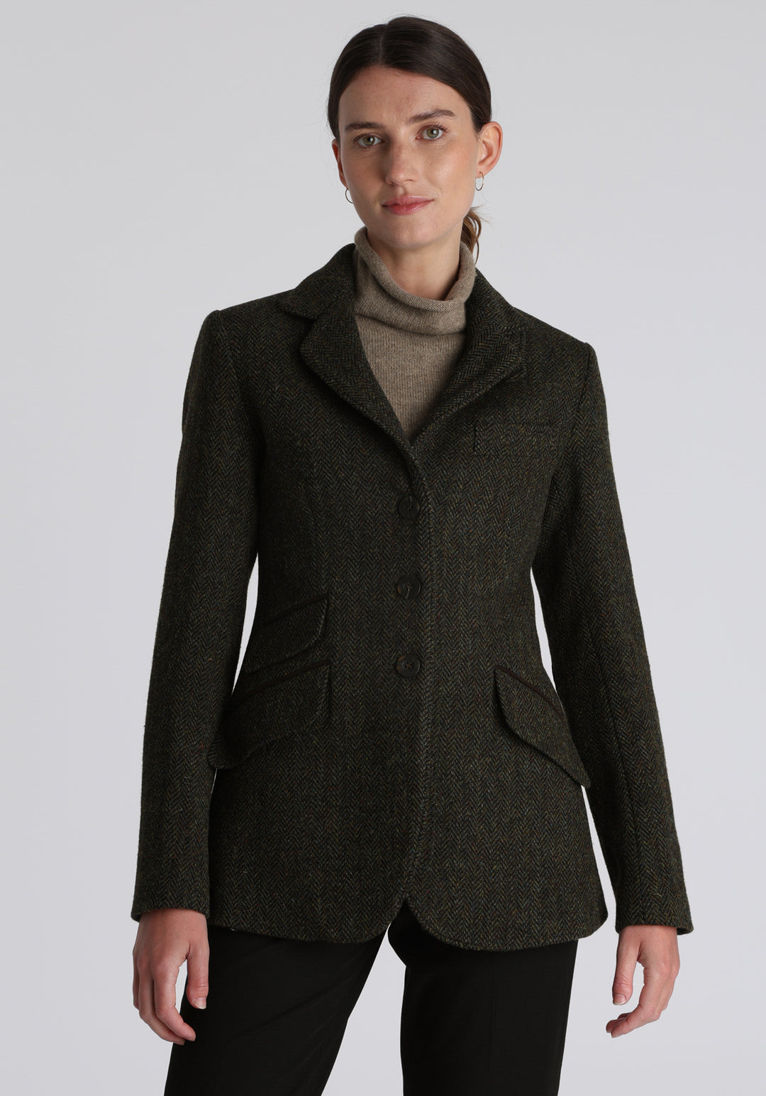 Model wearing the Patmos waistcoat in green spruce herringbone Harris Tweed with suede trim, a longline, neatly tailored style with a mandarin collar.