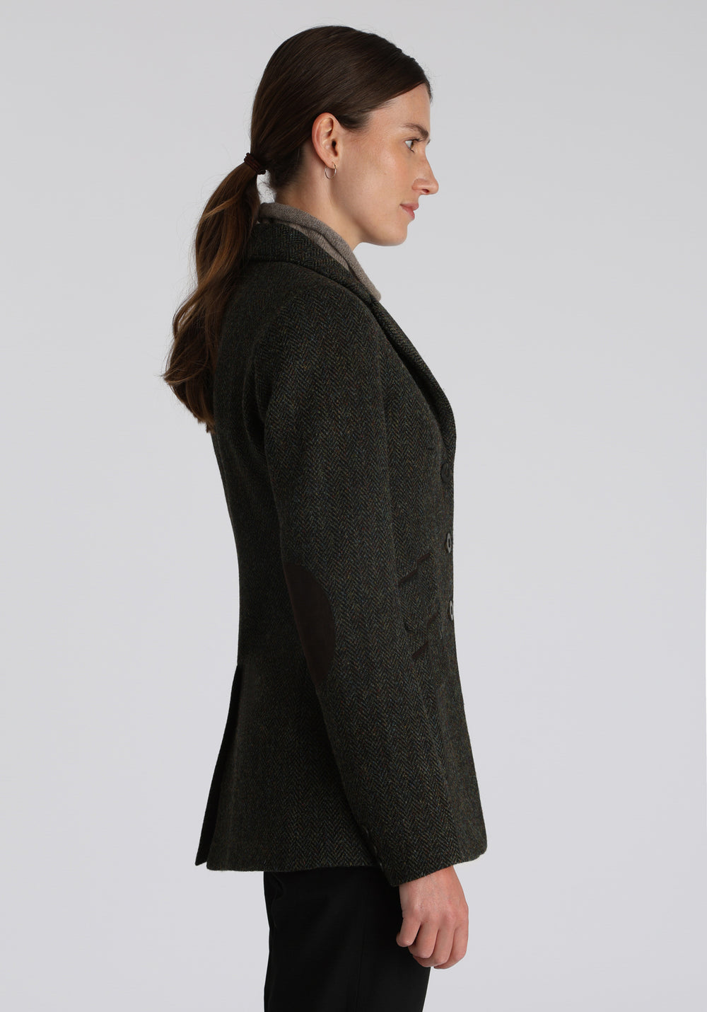 Model wearing the Patmos waistcoat in green spruce herringbone Harris Tweed with suede trim, a longline, neatly tailored style with a mandarin collar.