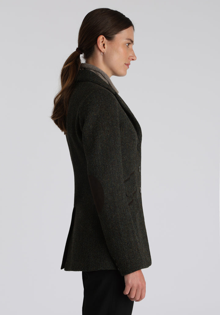 Model wearing the Patmos waistcoat in green spruce herringbone Harris Tweed with suede trim, a longline, neatly tailored style with a mandarin collar.