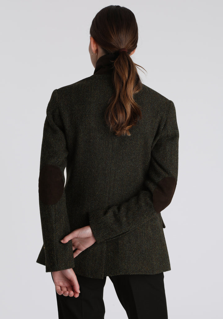 Model wearing the Patmos waistcoat in green spruce herringbone Harris Tweed with suede trim, a longline, neatly tailored style with a mandarin collar.