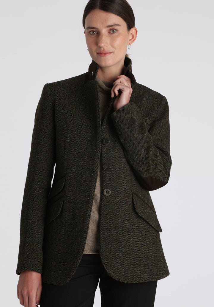 Model wearing the Patmos waistcoat in green spruce herringbone Harris Tweed with suede trim, a longline, neatly tailored style with a mandarin collar.